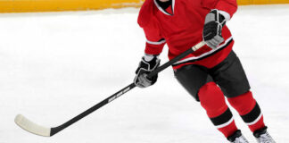 Hockey player in red jersey skating with puck.