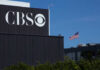 CBS sign on building, American flag in background.