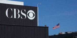 CBS sign on building, American flag in background.
