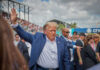 Man in blue suit waving in a crowd outdoors