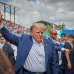 Man in blue suit waving in a crowd outdoors
