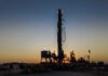 Drilling rig silhouetted against a sunset with workers visible