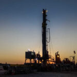 Drilling rig silhouetted against a sunset with workers visible