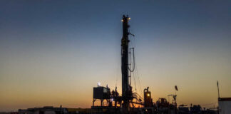 Drilling rig silhouetted against a sunset with workers visible