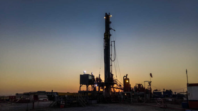 Drilling rig silhouetted against a sunset with workers visible