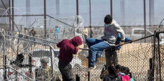 People climbing barbed wire fence wearing backpacks and hoodies