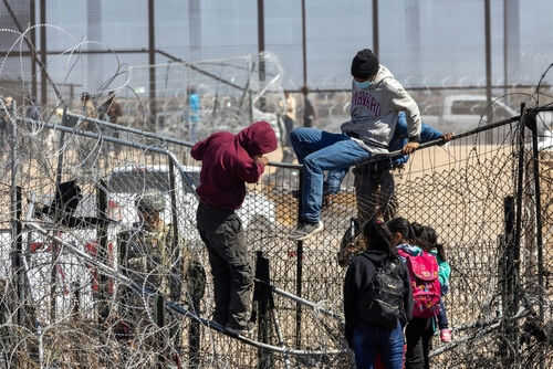 People climbing barbed wire fence wearing backpacks and hoodies