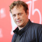 A man with curly hair poses at a film festival backdrop