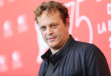A man with curly hair poses at a film festival backdrop