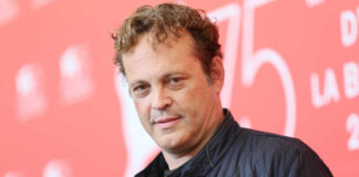 A man with curly hair poses at a film festival backdrop