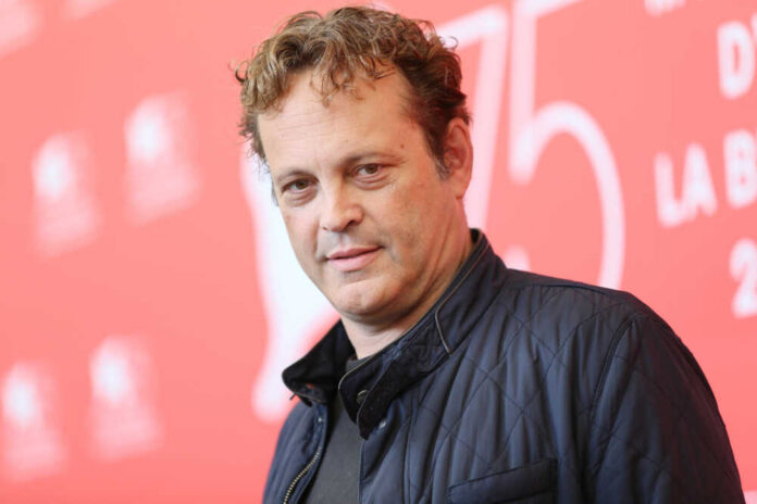A man with curly hair poses at a film festival backdrop