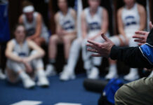A basketball coach speaking to a team in a locker room