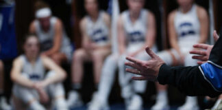 A basketball coach speaking to a team in a locker room