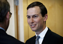 A man in a suit smiling while engaging in conversation indoors