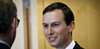A man in a suit smiling while engaging in conversation indoors