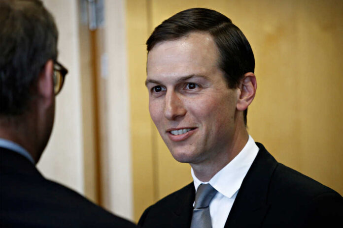 A man in a suit smiling while engaging in conversation indoors