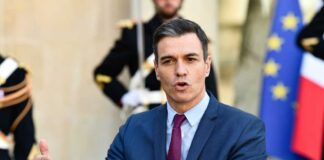 A government official delivering a speech outdoors with flags in the background