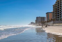 A beach with people walking along the shore and buildings in the background