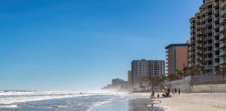 A beach with people walking along the shore and buildings in the background