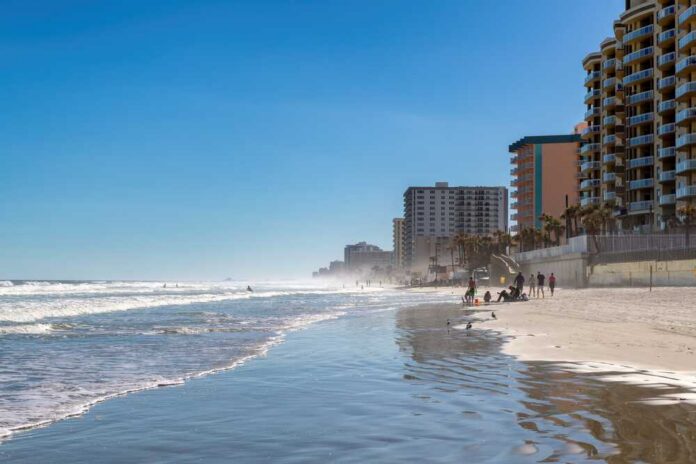 A beach with people walking along the shore and buildings in the background