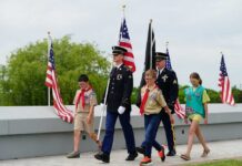 Children and military personnel participating in a memorial ceremony with flags