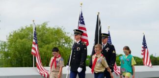 Children and military personnel participating in a memorial ceremony with flags