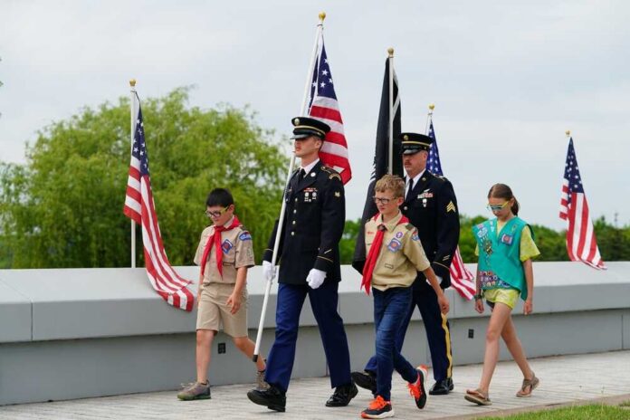 Children and military personnel participating in a memorial ceremony with flags