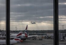 An airplane landing at an airport with other planes parked nearby