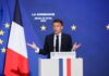 Emmanuel Macron delivering a speech at La Sorbonne with flags in the background