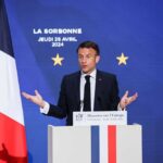 Emmanuel Macron delivering a speech at La Sorbonne with flags in the background
