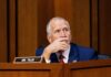 A politician sitting at a desk with a thoughtful expression during a hearing