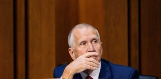 A politician sitting at a desk with a thoughtful expression during a hearing