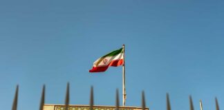 Iranian flag waving above a government building against a blue sky