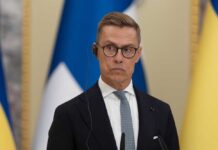 A man in formal attire wearing a headset during a press conference