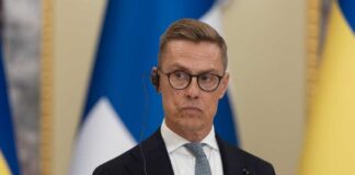 A man in formal attire wearing a headset during a press conference
