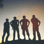 Silhouetted figures of four friends standing against a sunset