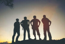 Silhouetted figures of four friends standing against a sunset