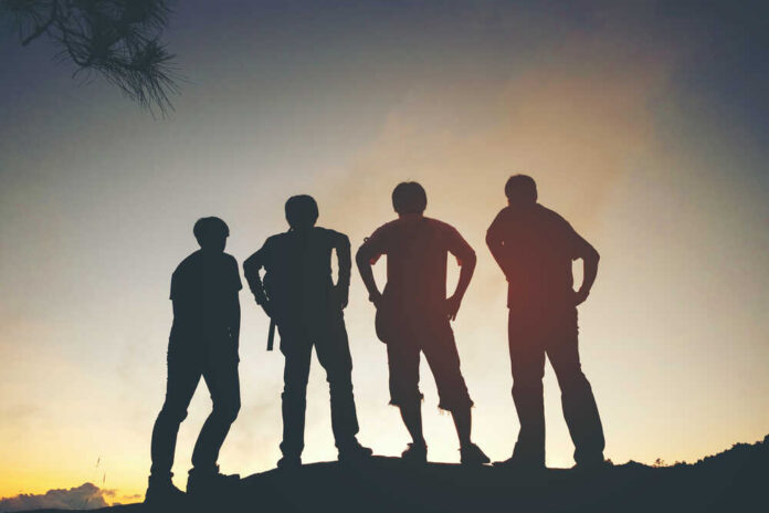 Silhouetted figures of four friends standing against a sunset