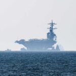 An aircraft carrier partially obscured by fog on the ocean