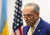 Schumer SLAMS Trump’s Iran Strategy Man in suit and glasses with flags in background