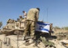 Soldiers on tank with Israeli flag in open field