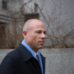 A man in business attire walking in an urban area with a serious expression