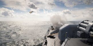 Naval ship firing a weapon into the ocean with a plane flying overhead