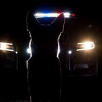 Silhouette of a police dog in front of a vehicle with emergency lights