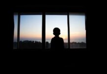 Silhouette of a child looking out a window at a sunset