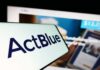 Close-up of a mobile device displaying the ActBlue logo with a blurred background of a fundraising website