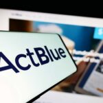 Close-up of a mobile device displaying the ActBlue logo with a blurred background of a fundraising website