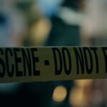 Caution tape marking a crime scene with blurred figures in the background