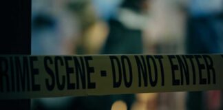 Caution tape marking a crime scene with blurred figures in the background