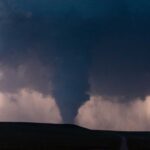 A tornado forming under dark storm clouds with lightning in the background